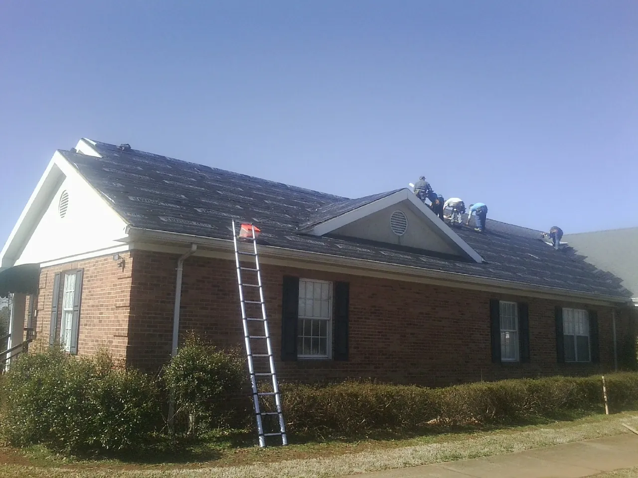 Crew tearing shingles off a brick ranch roof with a ladder set — Emergency Roof Repair work by our crew in Thompson