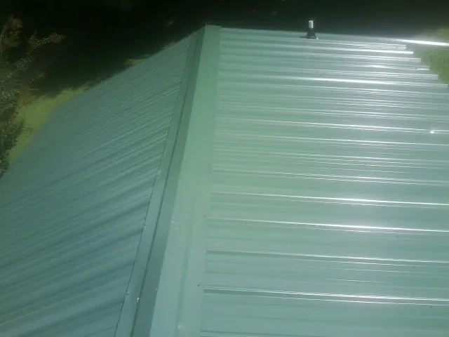 New green metal panels meeting at the ridge of a roof — Flat Roof Repair work by our crew in Thompson
